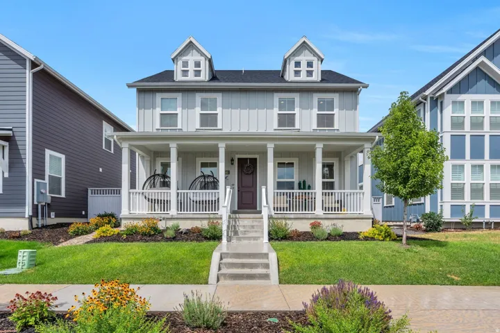 Two-story residence featuring light gray vertical siding, a covered front porch with white railings, and two dormer windows
