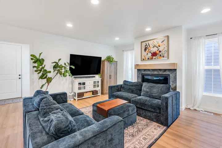 Spacious living room featuring recessed ceiling lighting, a gas fireplace with wood mantel surround, hardwood flooring, and large windows with plantation shutters