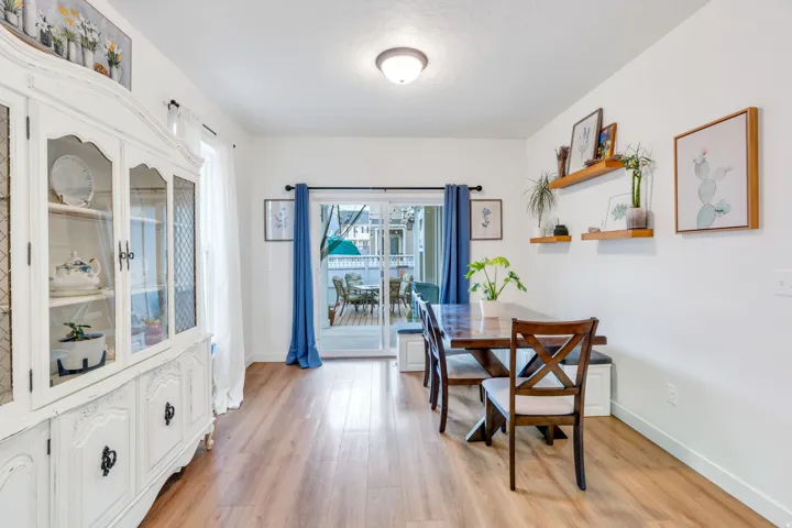 Bright dining area featuring wood-finish flooring, a blue-curtained glass door leading to outdoor space, white cabinetry with glass-front doors, and built-in shelving with decorative accents