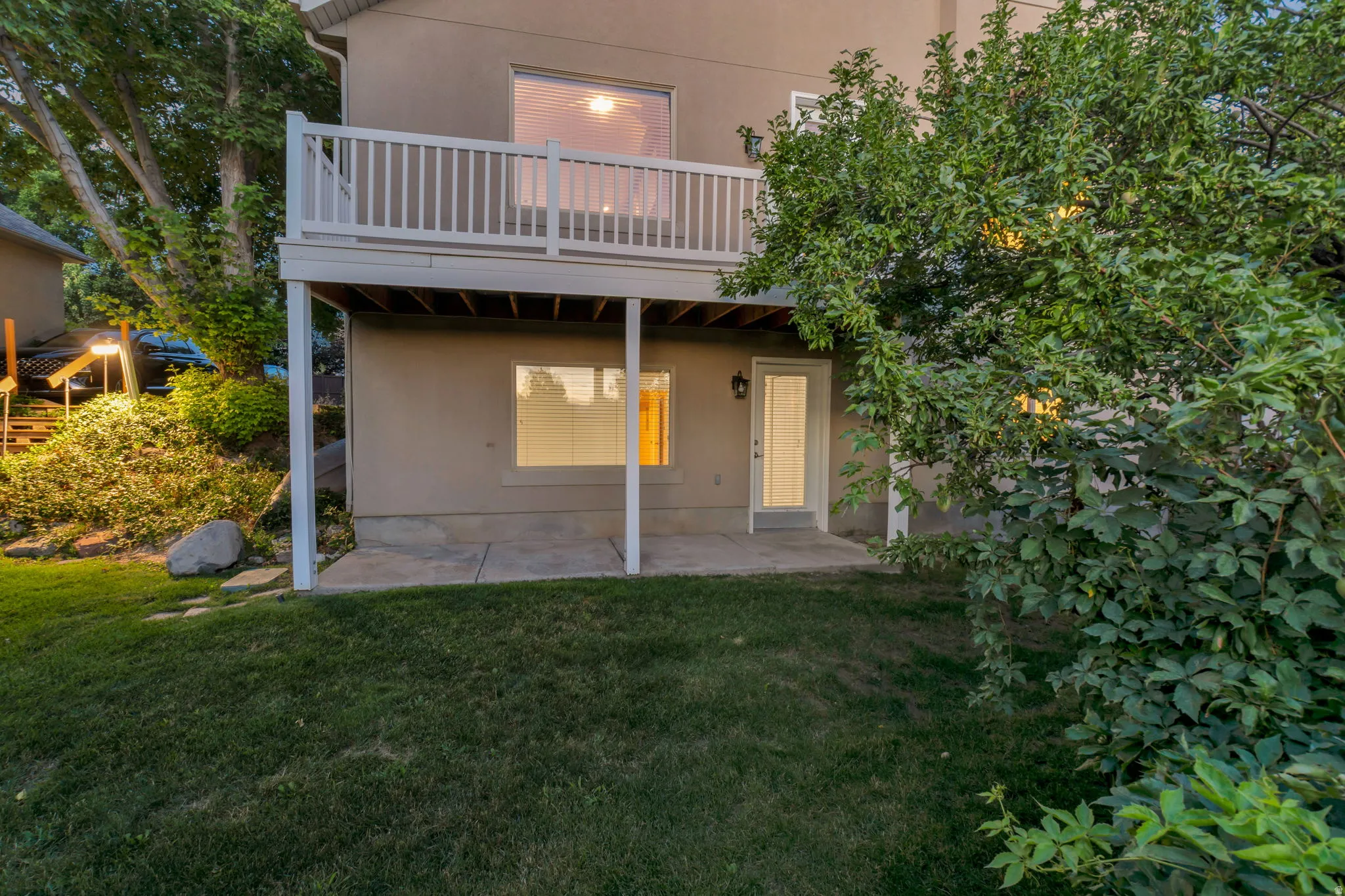 Exterior featuring a white-railed upper-level deck, a concrete patio, a ground-level door with a glass insert, and a surrounding lawn