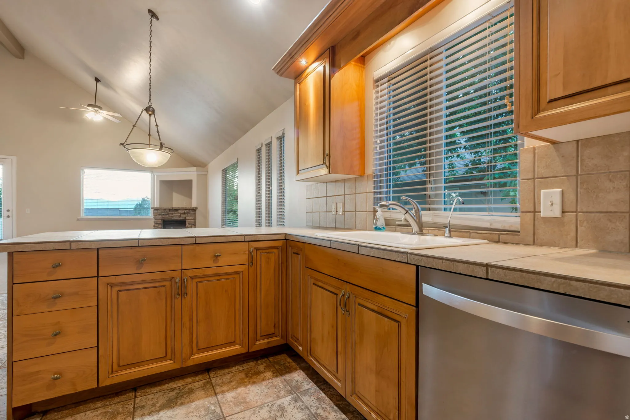Vaulted ceiling featuring a ceiling fan and pendant light fixture, wood cabinetry, tile flooring, and a stainless steel dishwasher