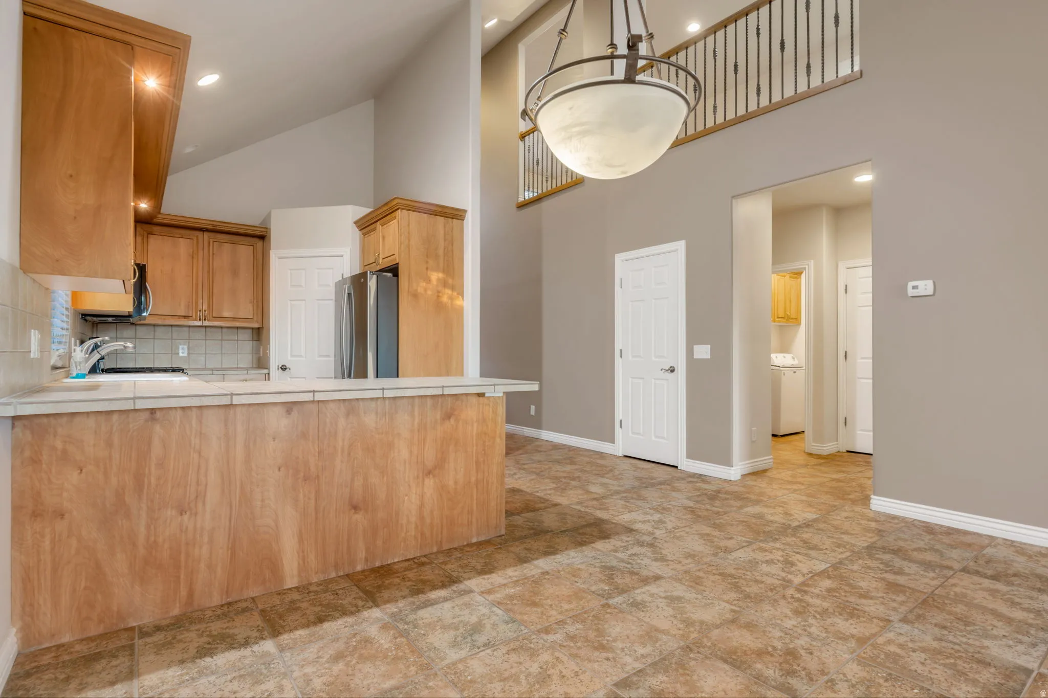 Vaulted ceilings, a kitchen island with tile countertop, wood-finish cabinetry, tile flooring, and an upper-level railing with metal spindles