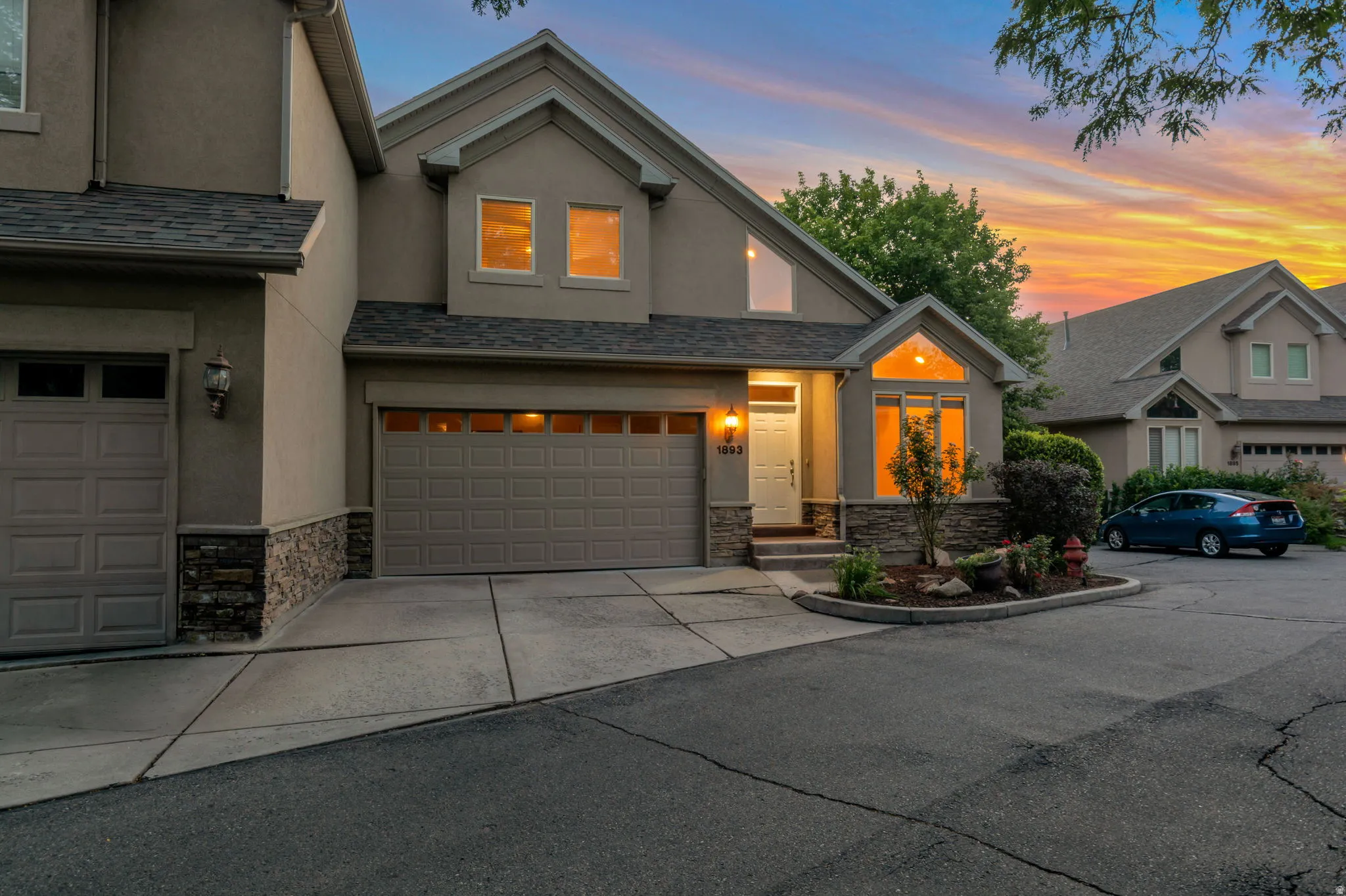 Stucco exterior with stone accents, attached two-car garage, established landscaping, and a covered entry