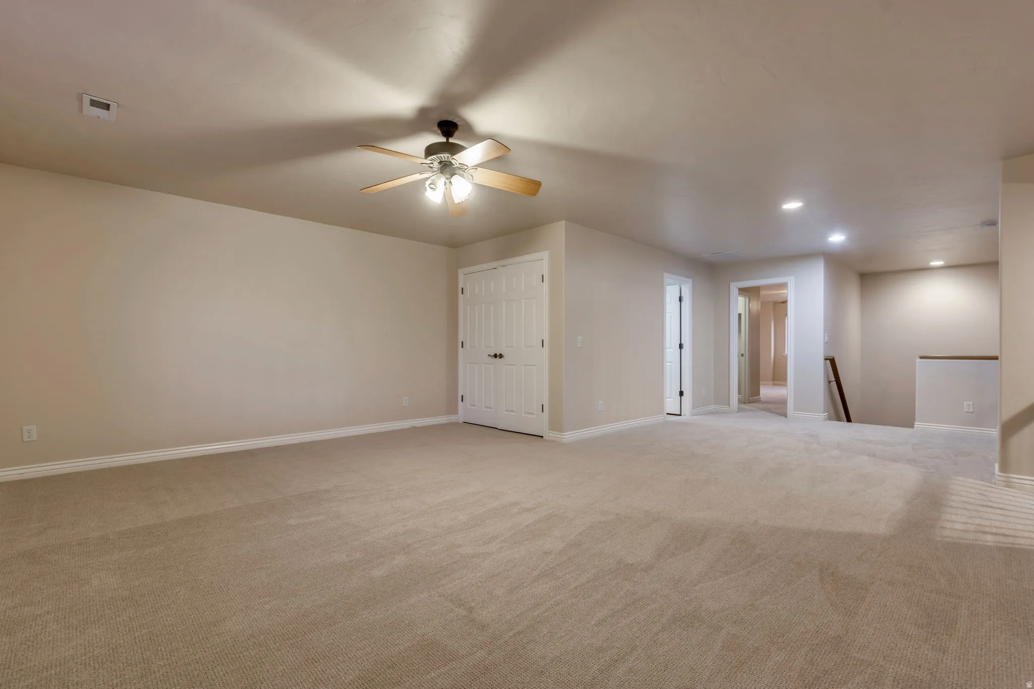 Expansive carpeted area featuring a ceiling fan, recessed lighting, and a white paneled door