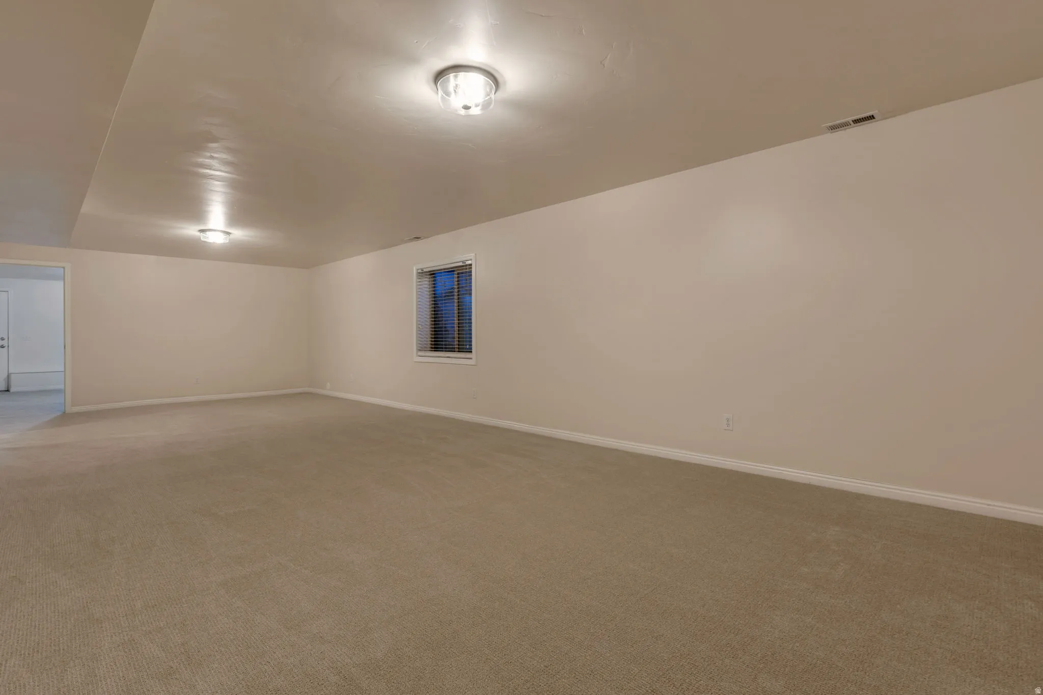Expansive open room featuring neutral carpet flooring, recessed window, and flush mount ceiling lights