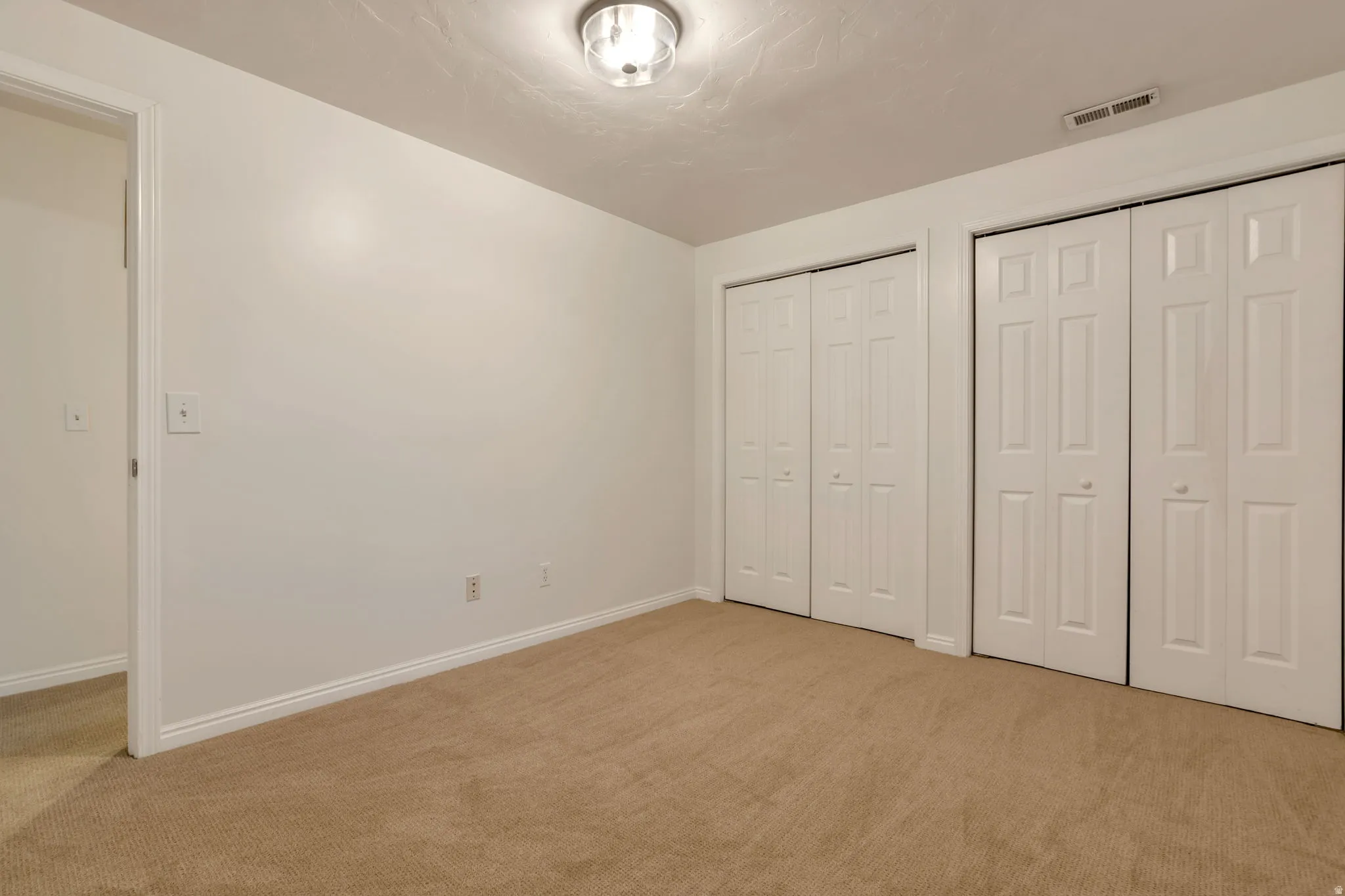Wall-to-wall carpeting, dual bi-fold closet doors, white trim, and a flush mount ceiling light fixture