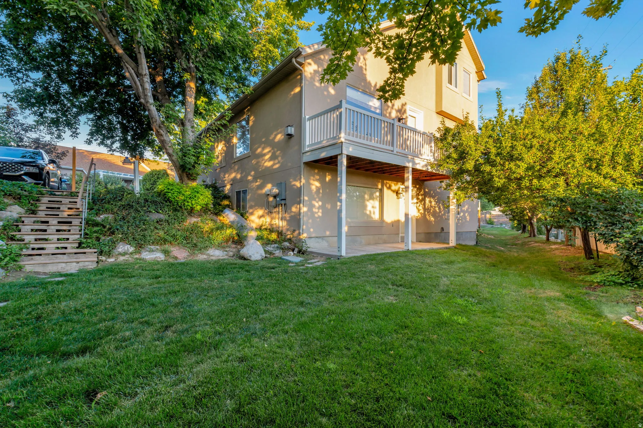 Expansive green lawn with mature trees, a multi-level deck, and a lower-level patio