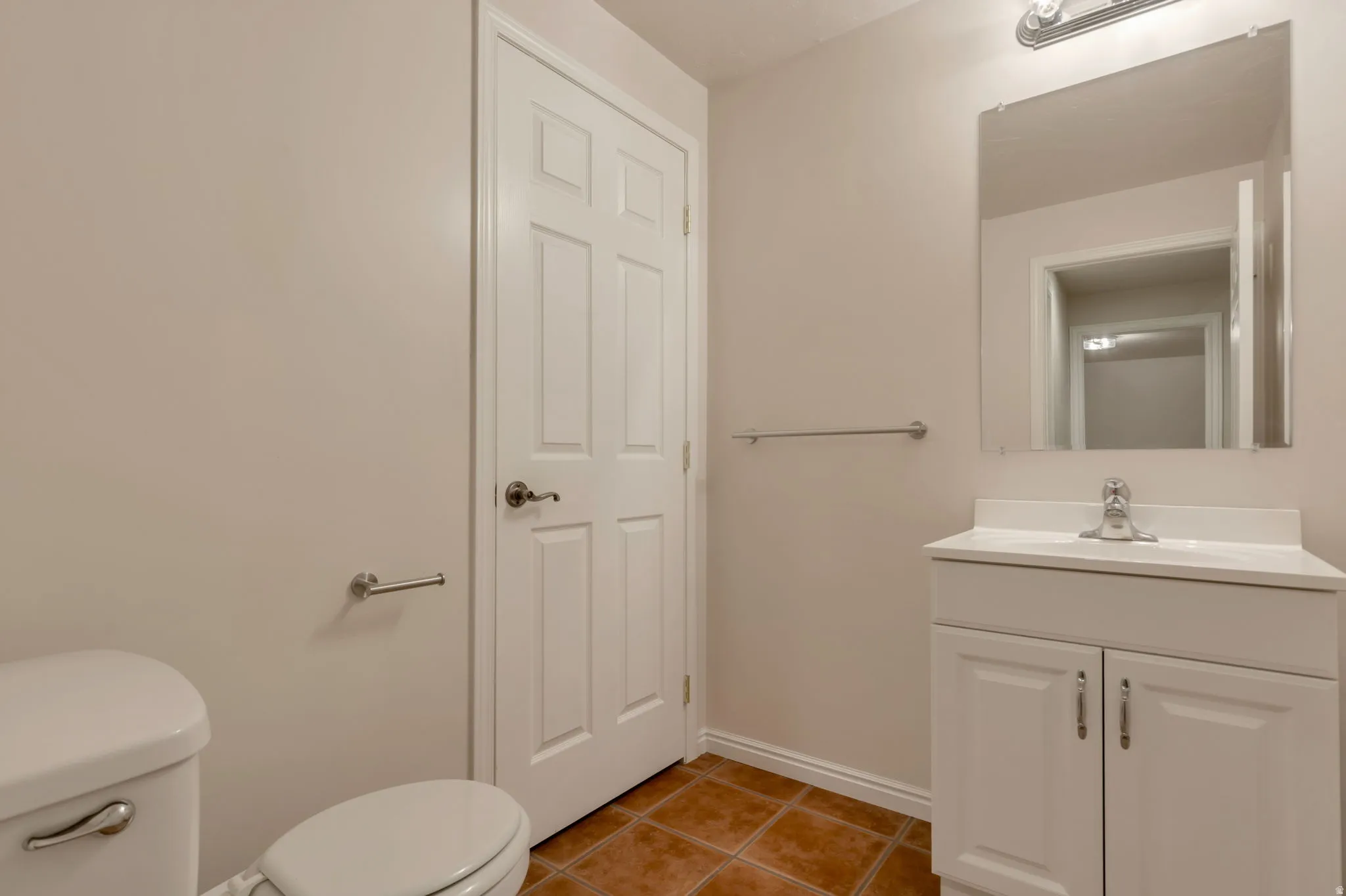White paneled door, ceramic tile flooring, white vanity with integrated sink, chrome faucet, and rectangular mirror with overhead lighting