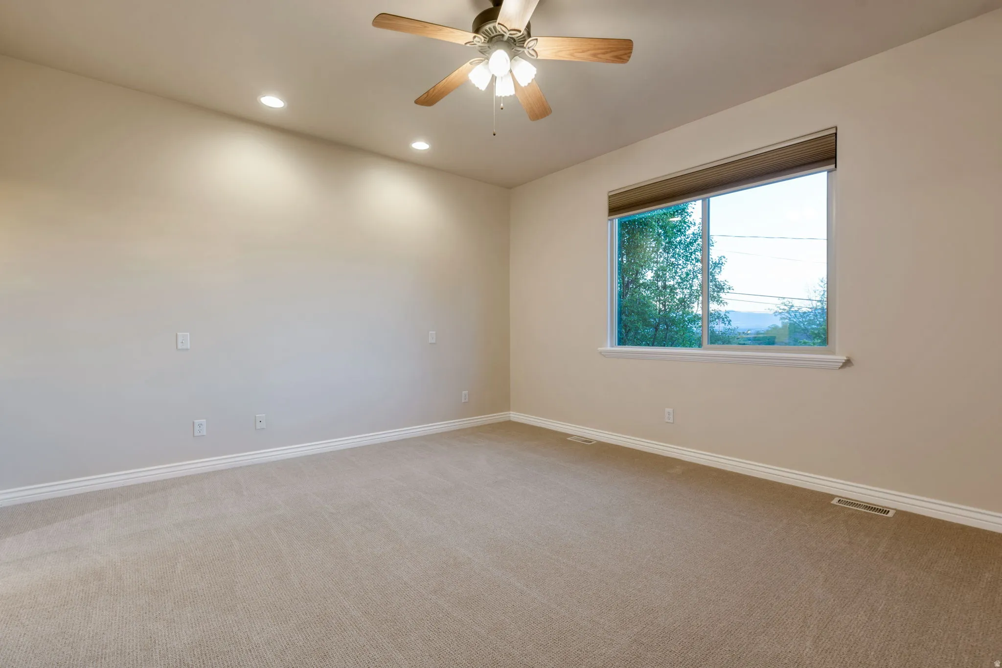 Recessed lighting and a ceiling fan fixture illuminate a carpeted room with a large window