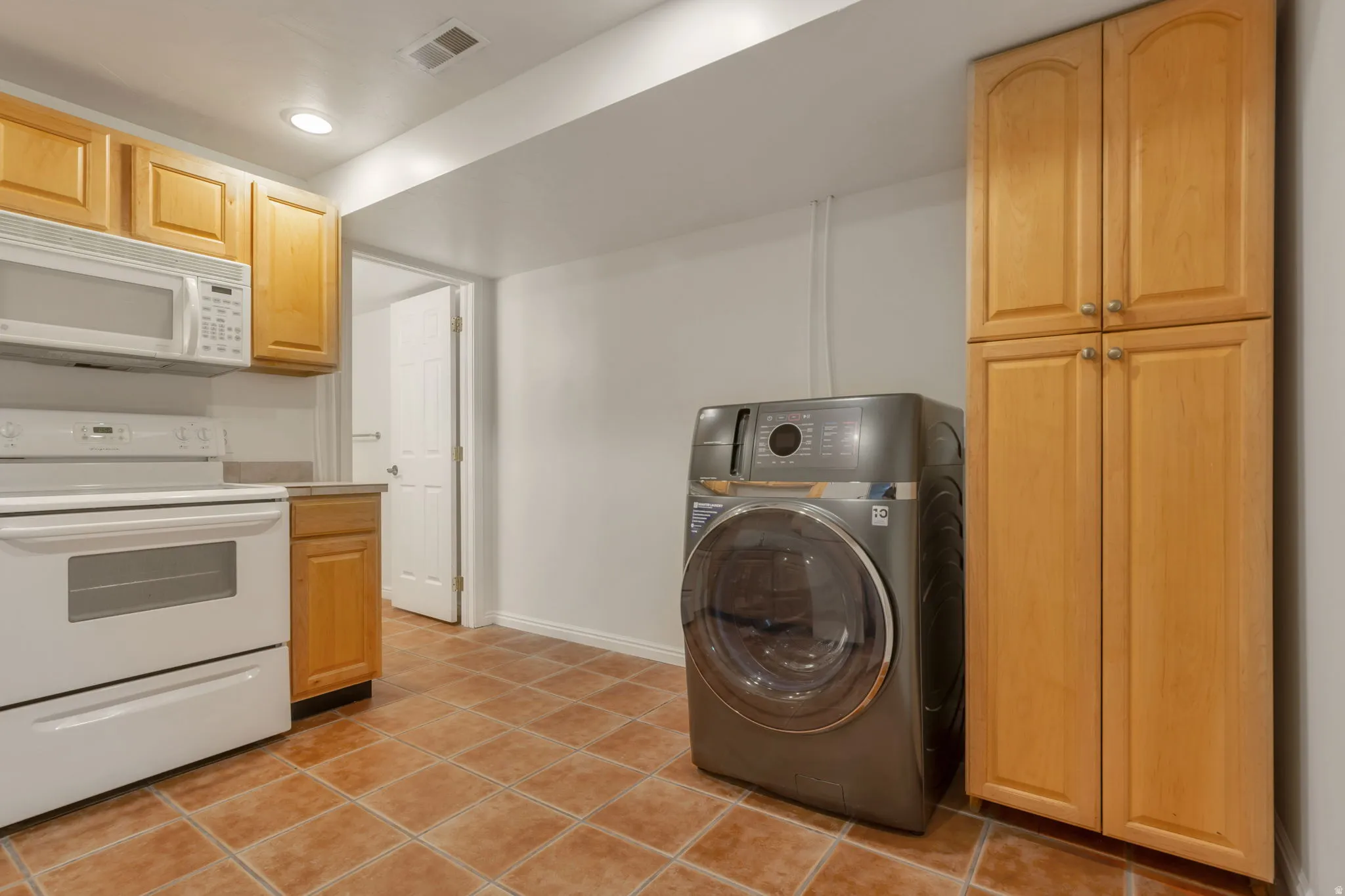 Kitchenette featuring wood cabinetry, white microwave, white electric range, and tile flooring