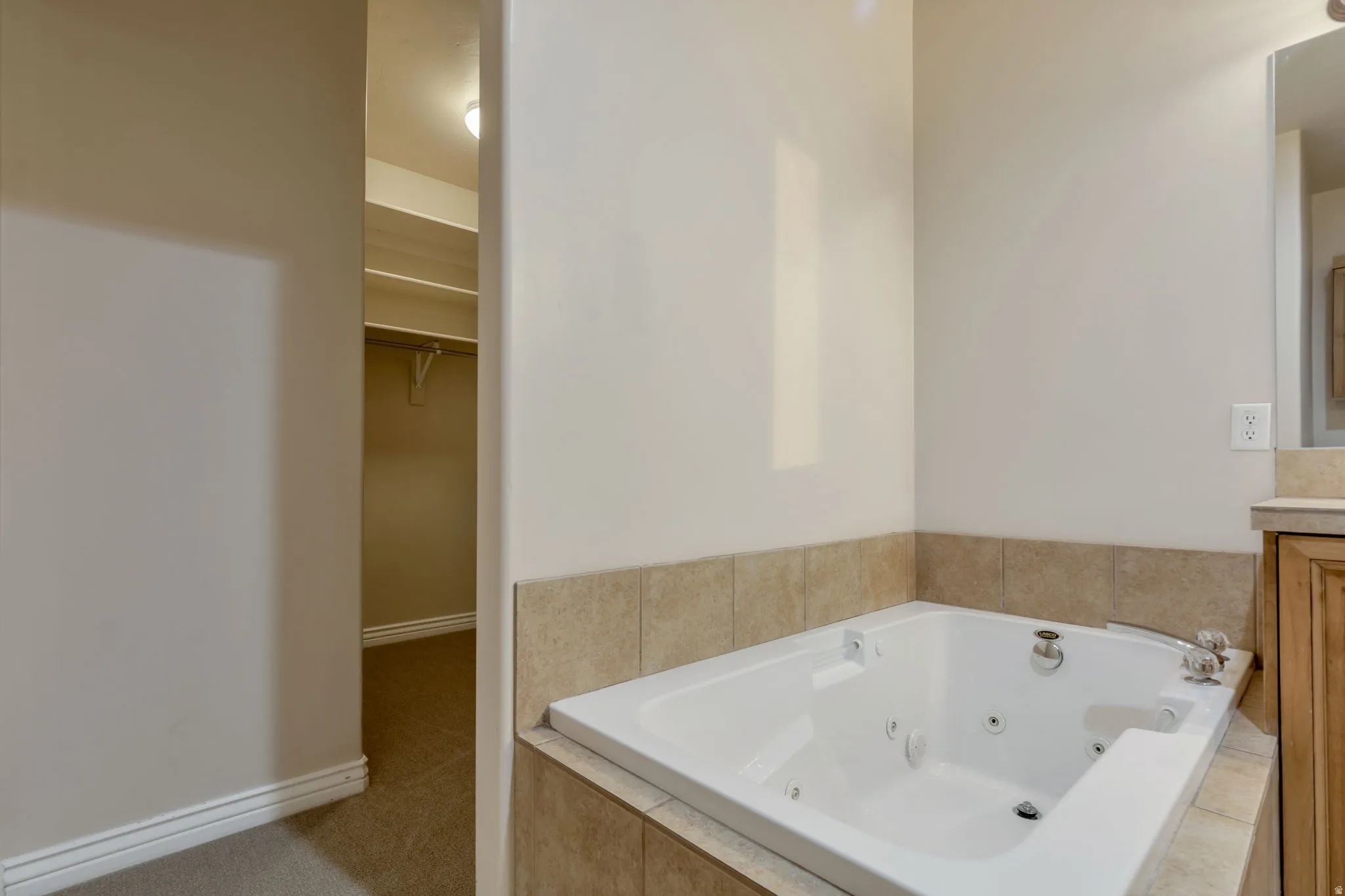 Built-in jetted tub with tile surround, wood-finish vanity with countertop, and recessed lighting