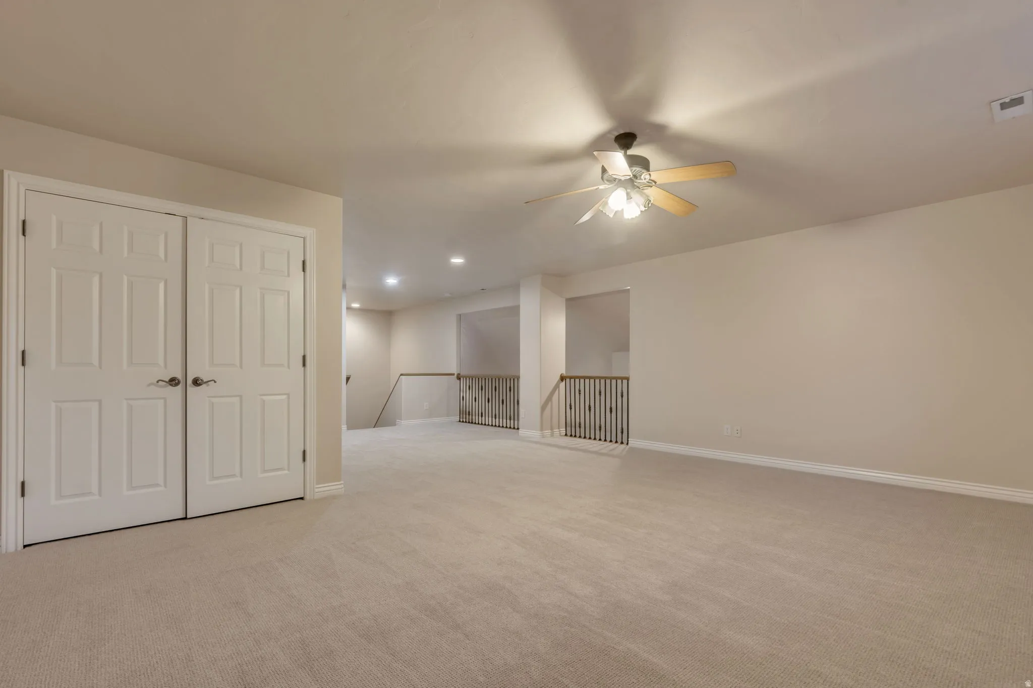 Spacious carpeted room featuring a ceiling fan with integrated lighting, recessed lighting, double panel doors, and a wrought iron railing