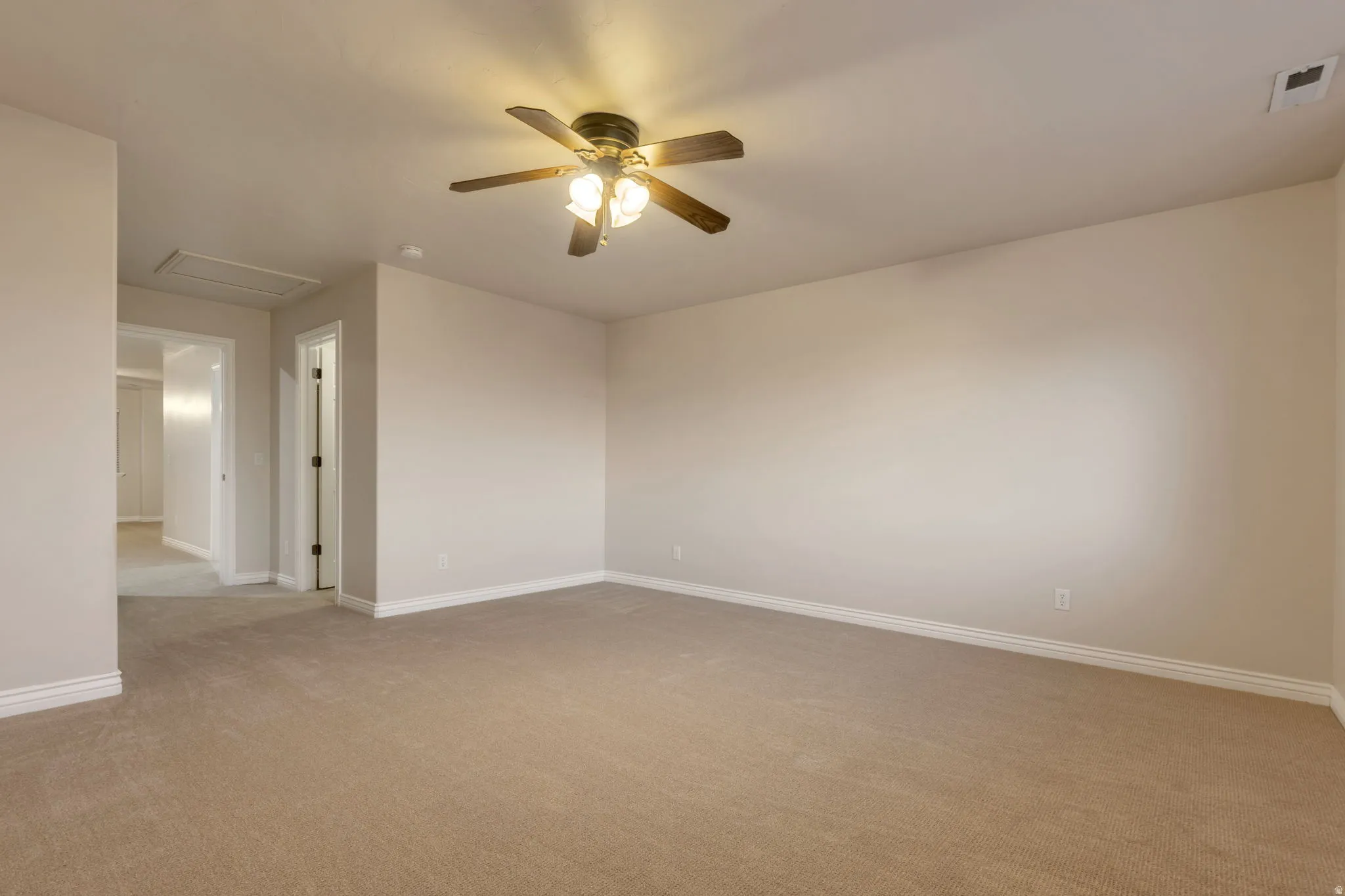 Expansive room featuring neutral-toned carpeting, a ceiling fan with integrated lighting, and light-colored walls
