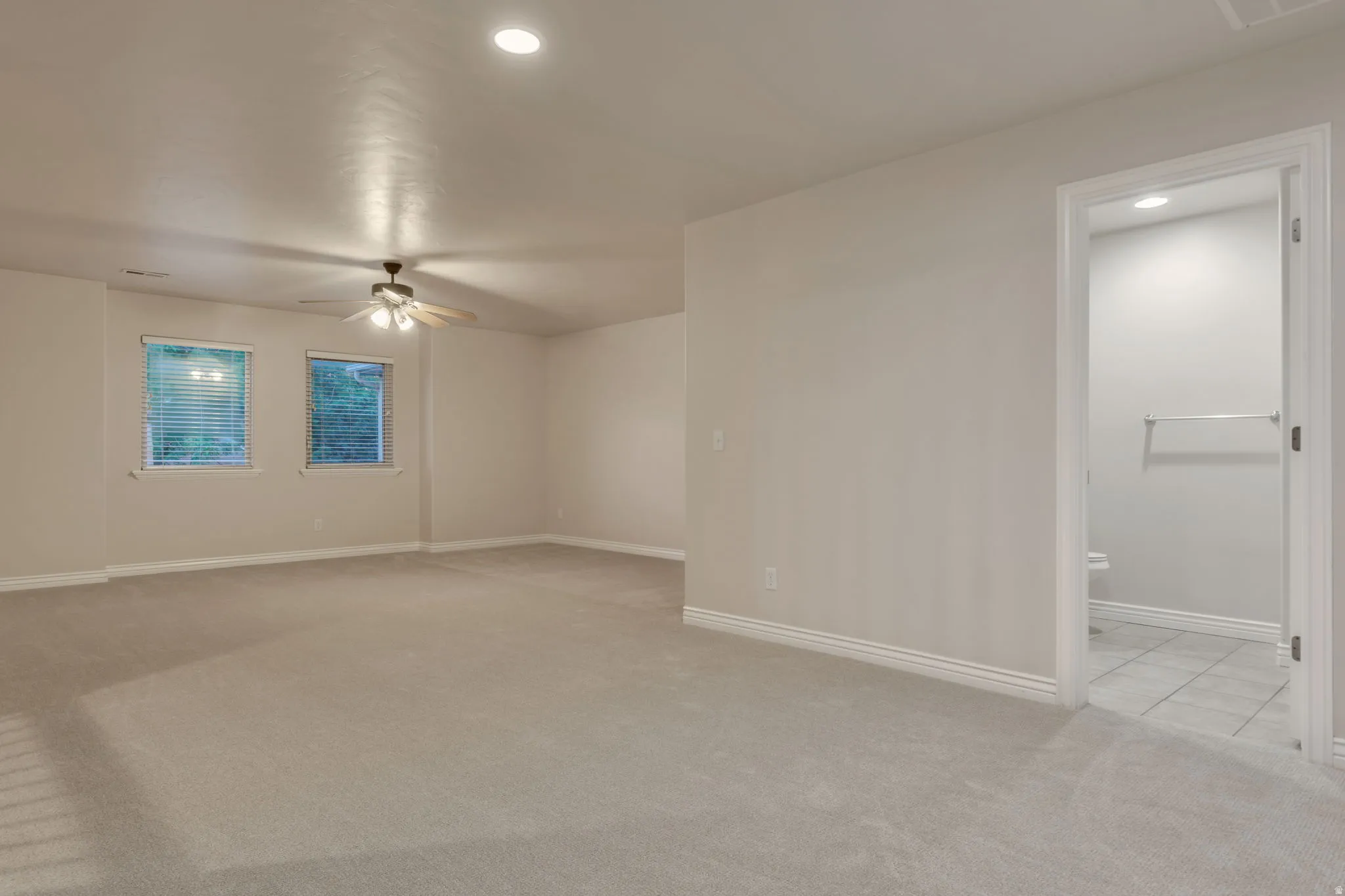 Spacious carpeted room with neutral paint, two windows with blinds, a ceiling fan, and recessed lighting