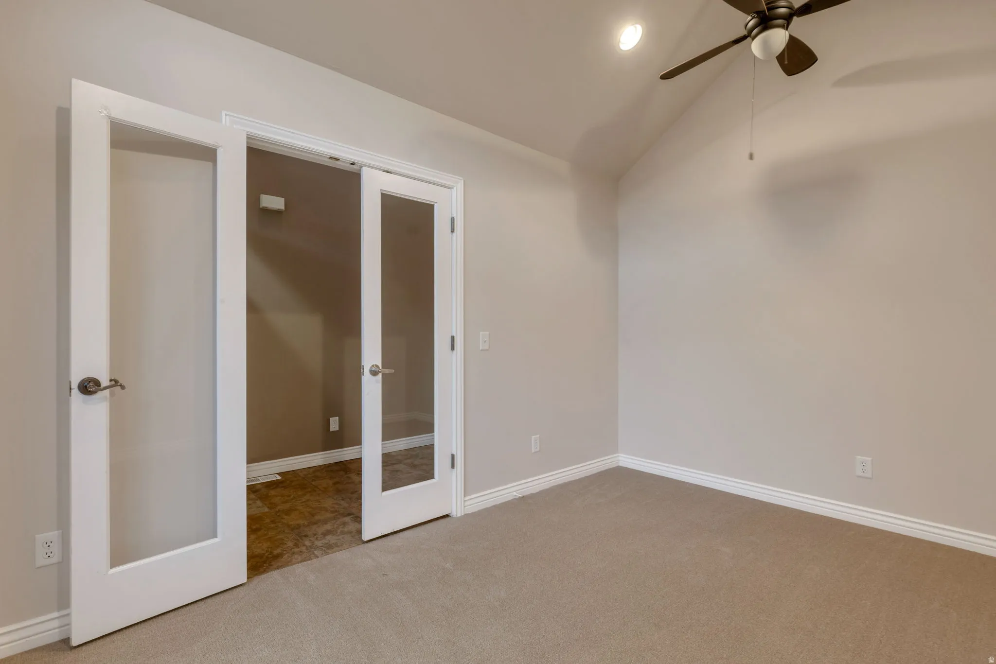 Vaulted ceiling, ceiling fan, neutral carpet, white trim, and French doors with privacy glass