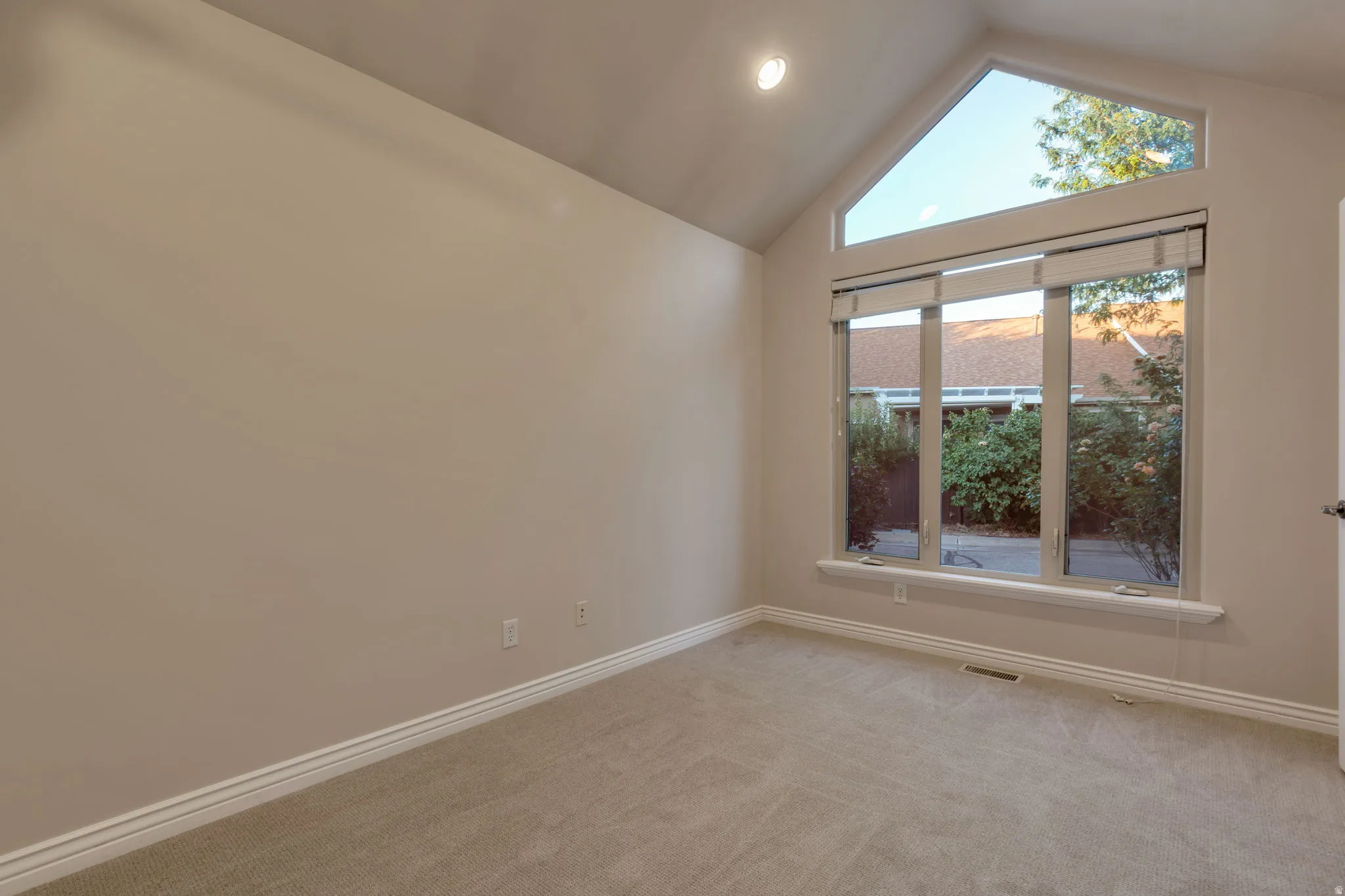 Pitched ceiling featuring an accent window, large multi-pane window with shades, neutral carpeting, and recessed lighting