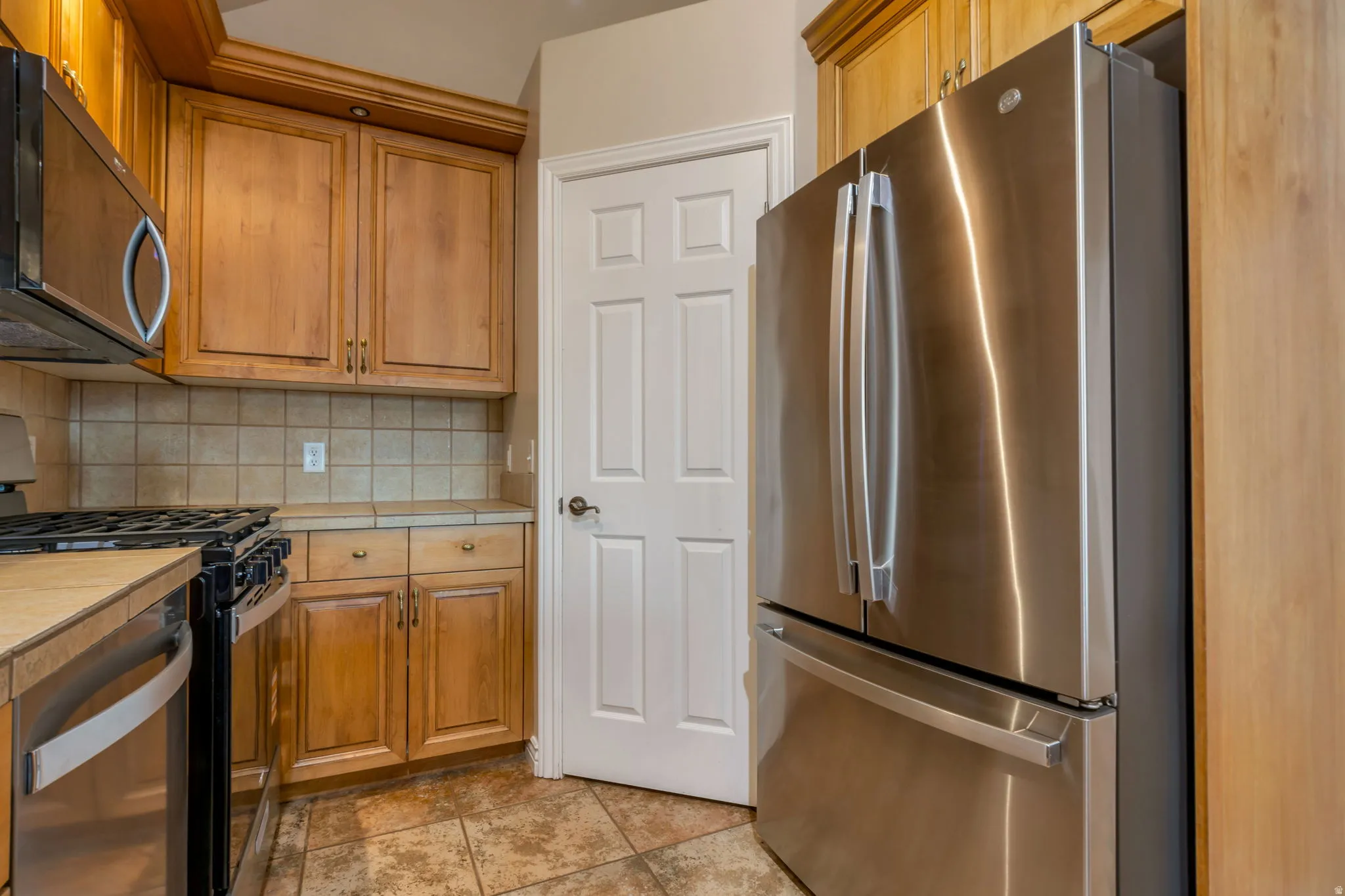 Stainless steel French door refrigerator, wood cabinetry, tile backsplash, built-in microwave, and stainless steel gas range
