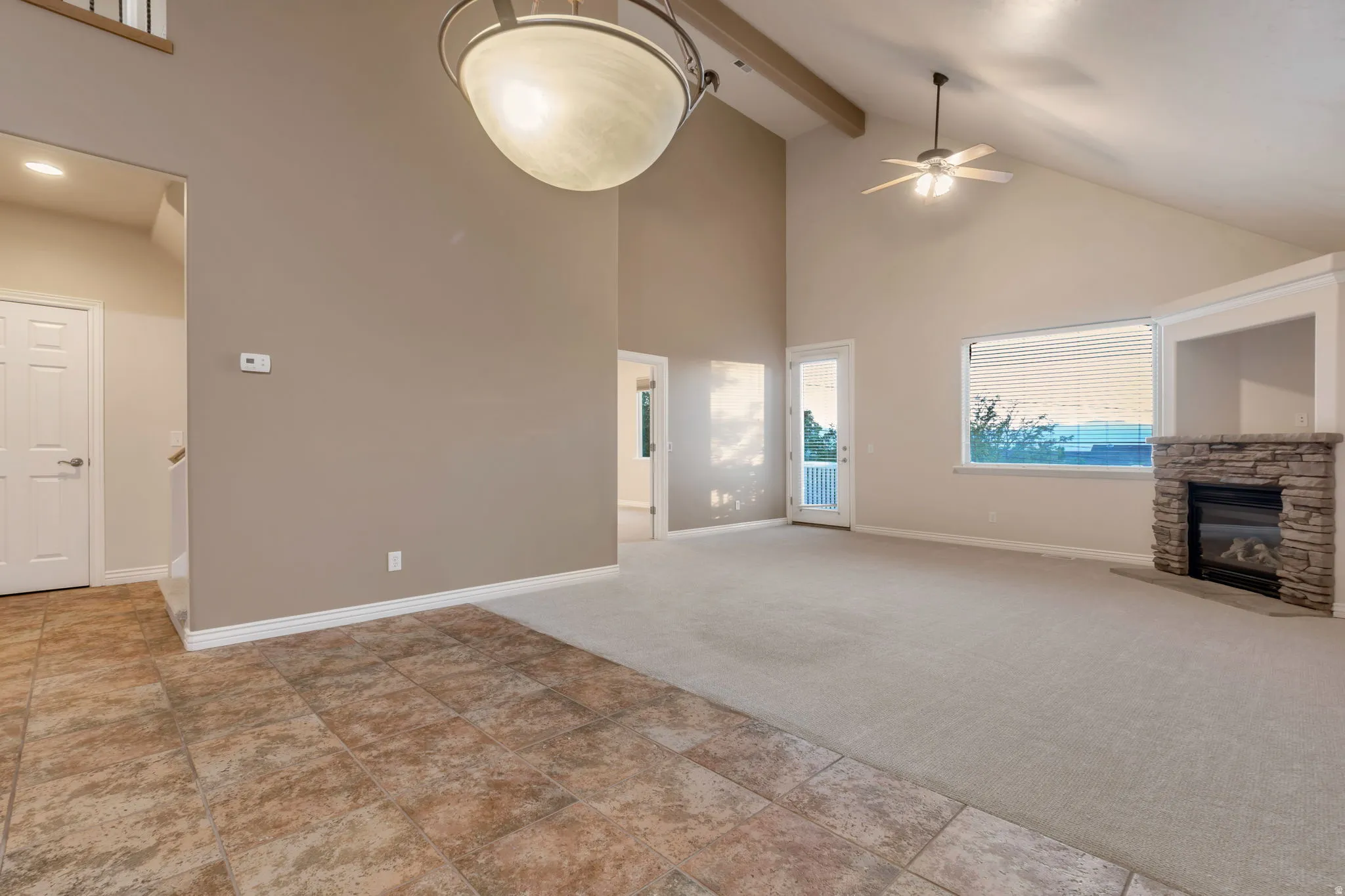 Vaulted ceiling with exposed beams, stone-clad fireplace, ceiling fan, and tiled entry