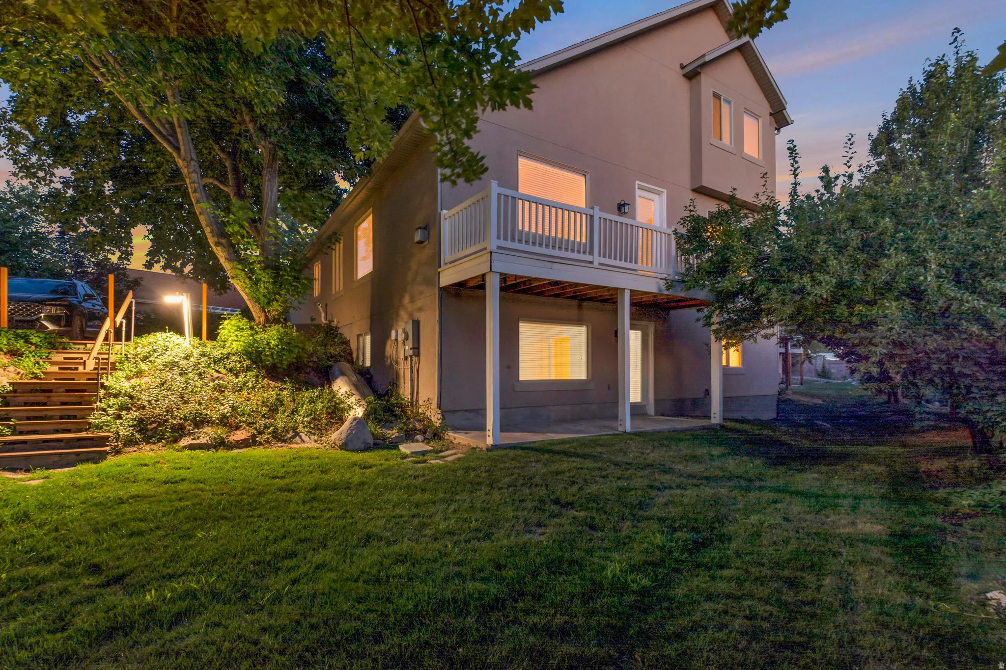 Two-story exterior with a second-level balcony, ground-level patio, and exterior lighting