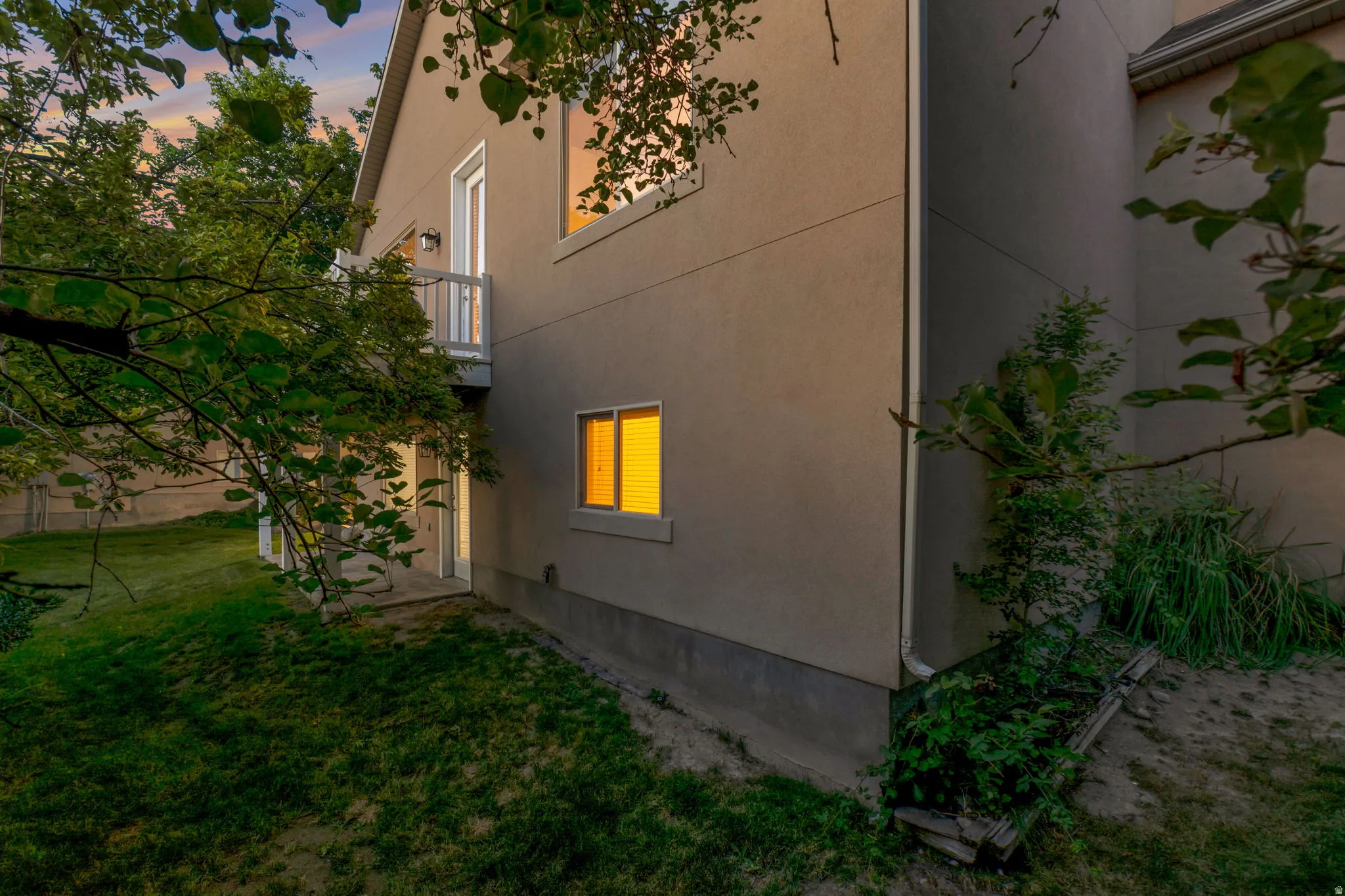 Stucco exterior with multiple windows, an upper-level balcony, and a lower-level patio door