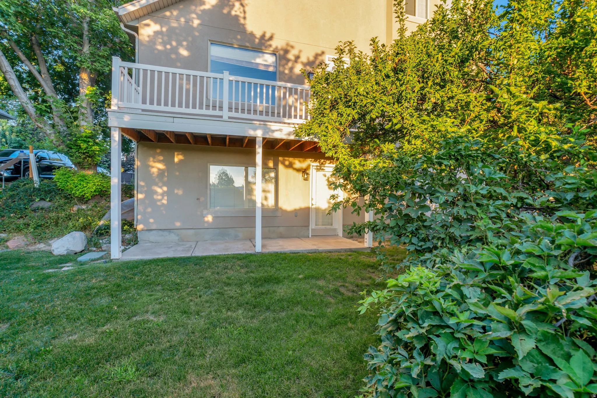 Rear facade with a second-story balcony featuring white railings, a ground-level patio, and surrounding mature landscaping