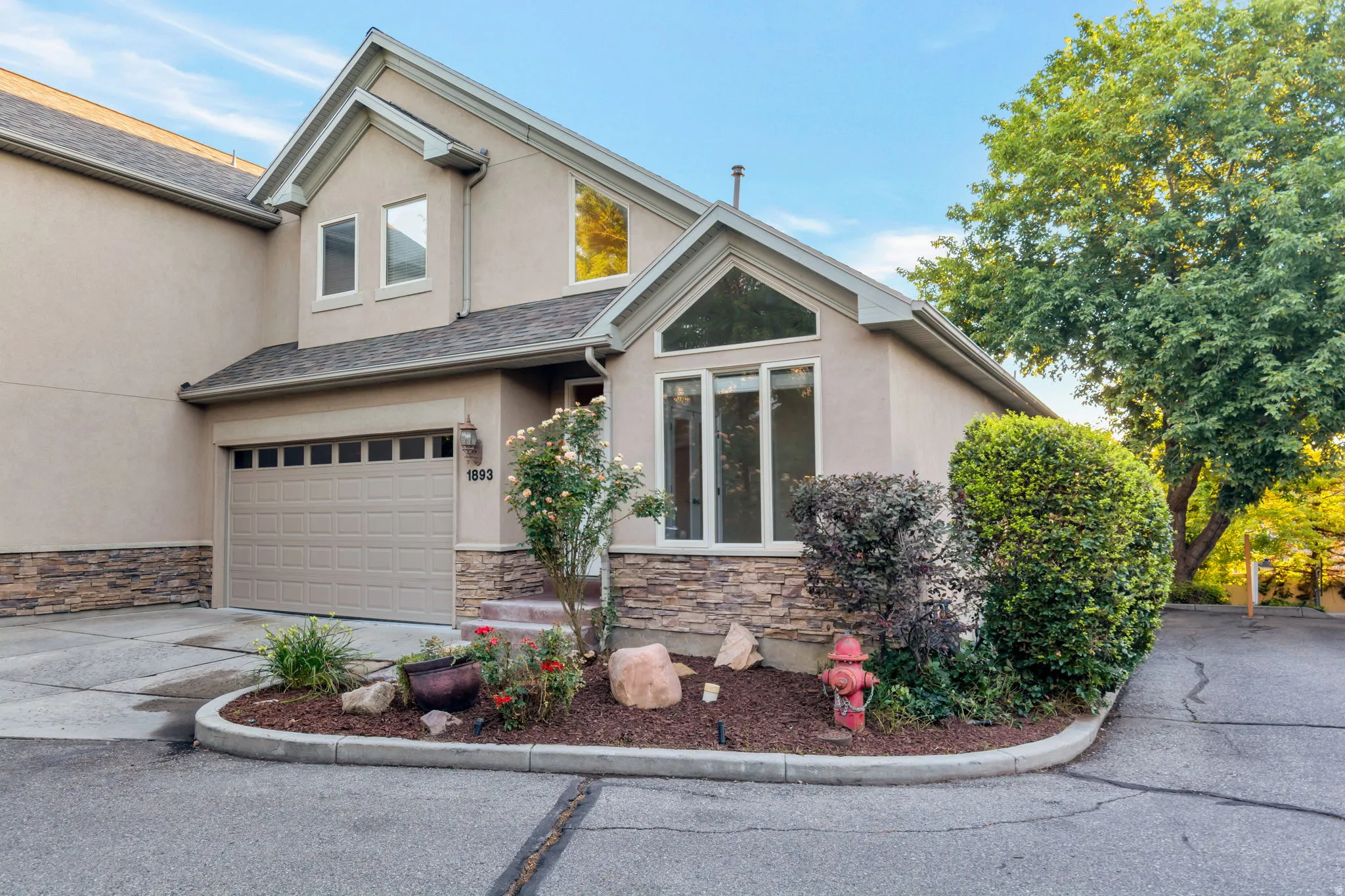 Stucco exterior with stone accent detailing, an integrated garage, and a landscaped entry with mature plantings