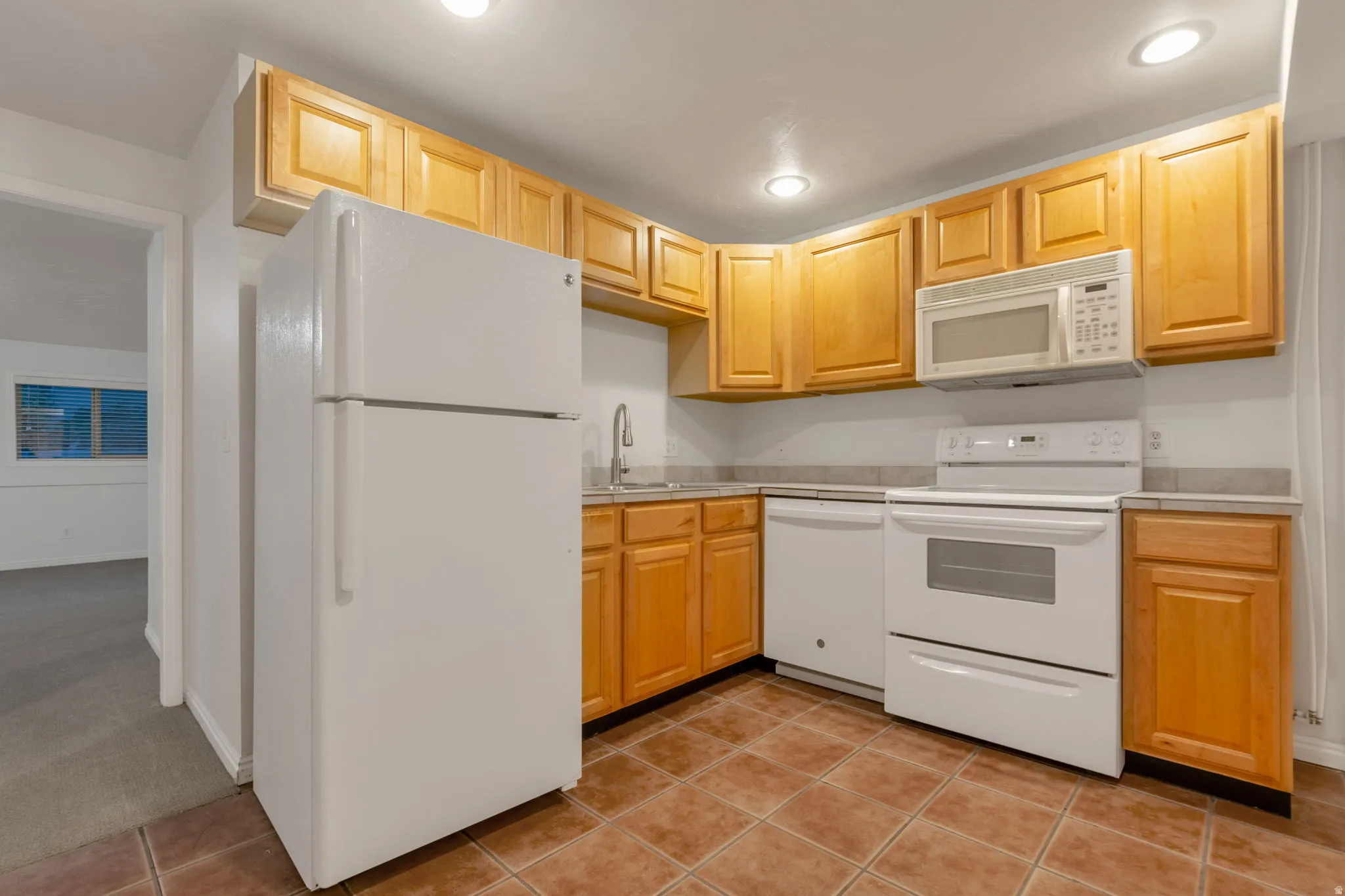 Kitchen featuring wood cabinetry, white appliances, recessed lighting, and tile flooring