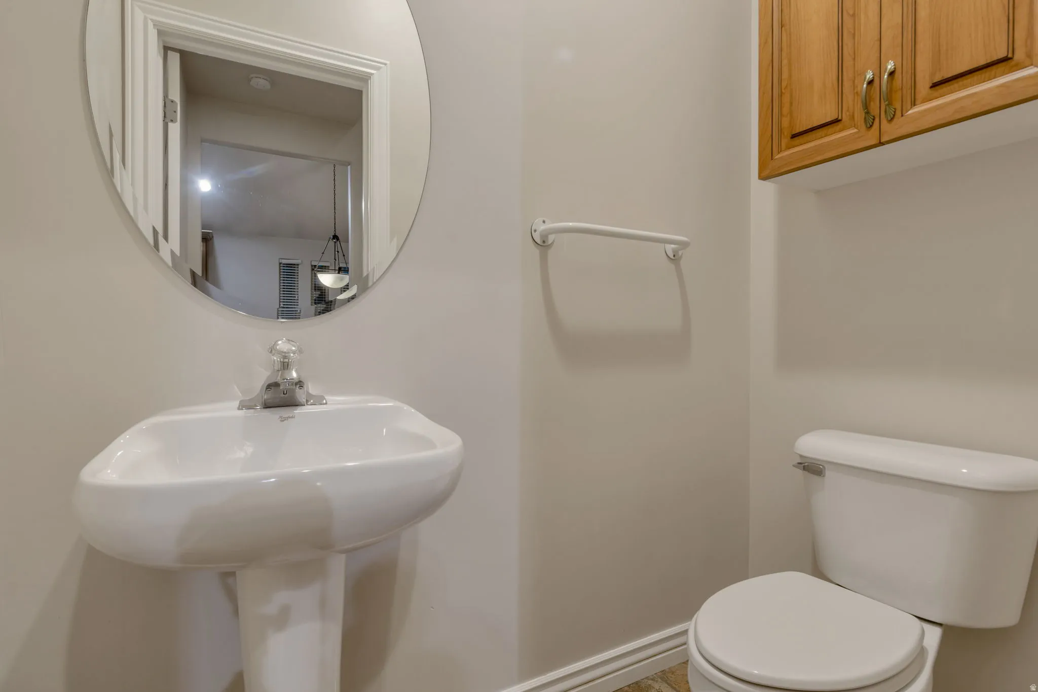 Pedestal sink with a polished chrome faucet, oval wall-mounted mirror, and wood-finish cabinetry