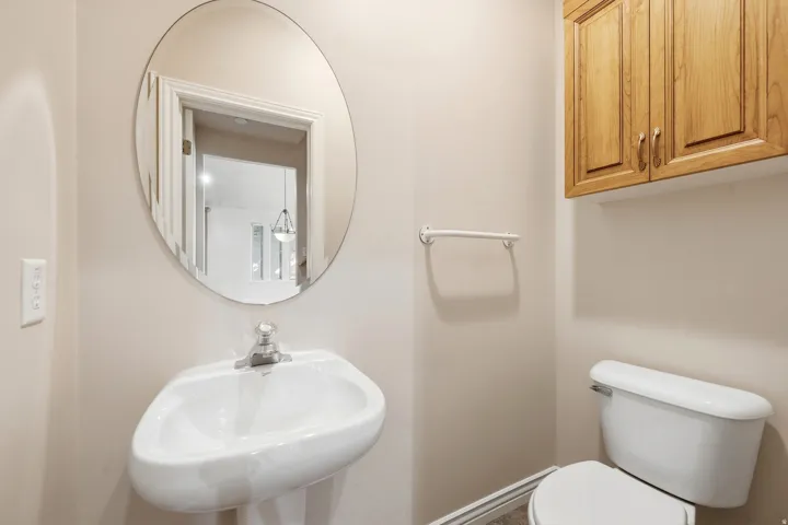 Pedestal sink with a polished chrome faucet, oval wall mirror, and light wood-finish cabinetry