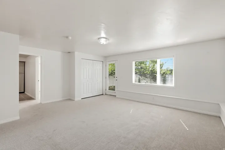 Neutral tone carpeting, white walls, double bi-fold closet doors, a single window with blinds, and a glass-paneled door