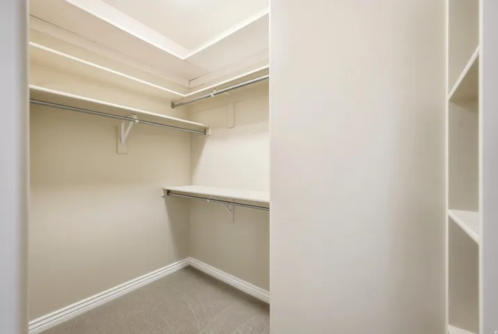 Walk-in closet with carpet flooring, built-in shelving, and multiple hanging rods