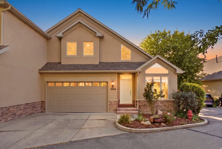 Stucco exterior with stone accents, attached garage, gabled roofline, front entry door, and landscaped front planting area