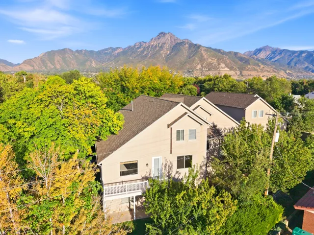 Multi-level exterior with a mountain backdrop, featuring a deck, multiple windows, and mature trees