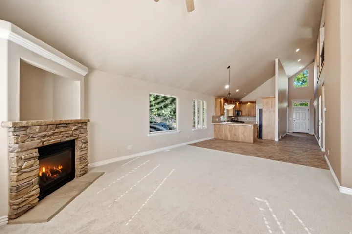 Stone-clad fireplace with mantel, vaulted ceilings, recessed lighting, wood-finish cabinetry, and a double front door with upper transom window