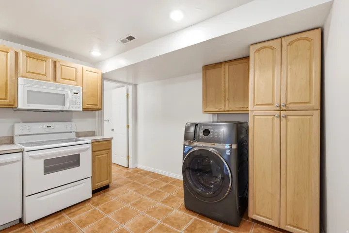 Full-size laundry appliance, wood-finish cabinetry, white over-range microwave, white electric range, and tiled flooring