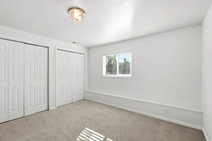 Neutral wall color, wall-to-wall carpeting, window with blinds, bi-fold closet doors, and flush-mount ceiling light fixture