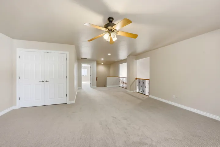Expansive carpeted room featuring a ceiling fan with integrated lighting, a double-door closet, and a wrought iron banister