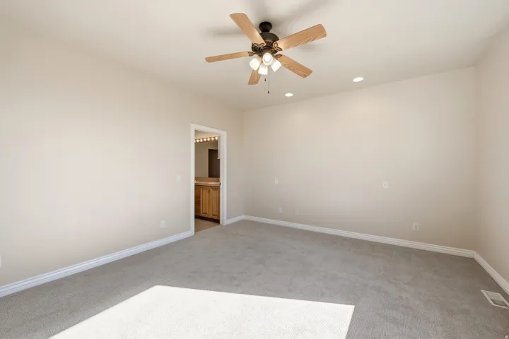 Neutral tone wall paint, recessed lighting, ceiling fan with light fixture, light gray carpeting, and a doorway revealing wood-finish cabinetry