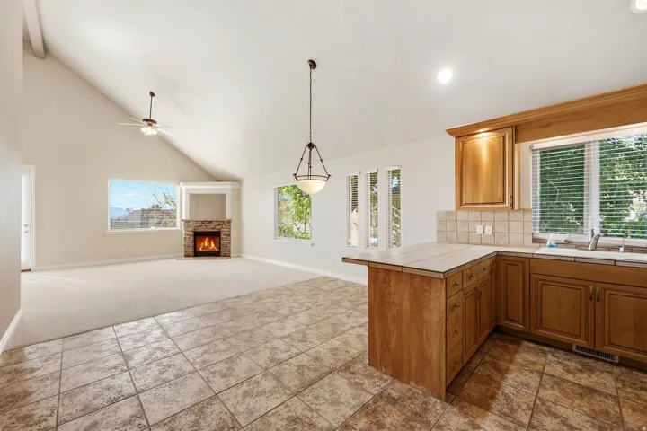 Vaulted ceiling, stone-clad fireplace, wood cabinetry, tile flooring, and a ceiling fan