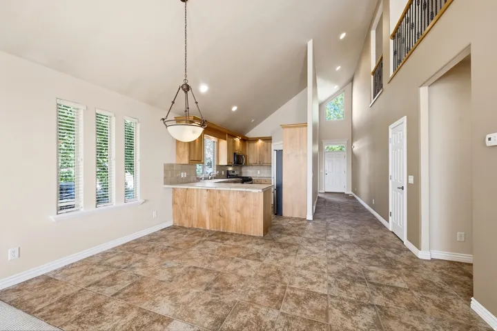 Vaulted ceilings, tiled flooring, wood-finish cabinetry, stainless steel appliances, and a wrought iron banister