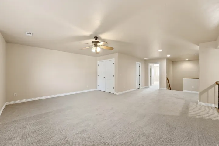 Expansive carpeted area featuring a ceiling fan with integrated lighting, recessed lighting, double closet doors, and wood newel posts with iron balusters