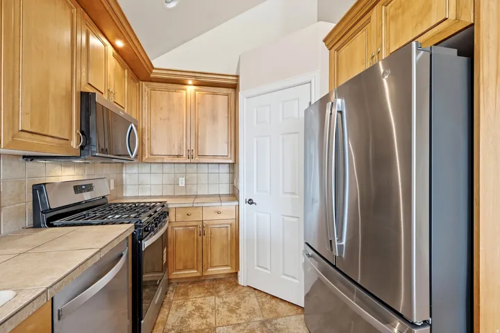 Kitchen featuring wood cabinetry, stainless steel appliances, tile flooring, and a tile backsplash