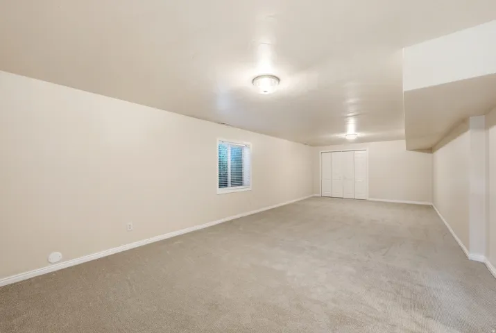 Spacious room featuring neutral carpeting, a single window with blinds, and bi-fold closet doors