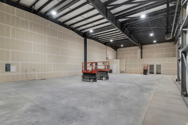 Expansive interior space featuring concrete flooring, unpainted drywall, exposed steel beam construction, and recessed ceiling lighting