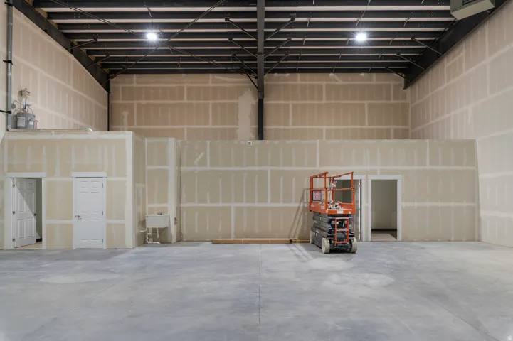 Spacious interior with exposed steel beam ceiling, high ceilings, concrete flooring, and multiple interior doorways