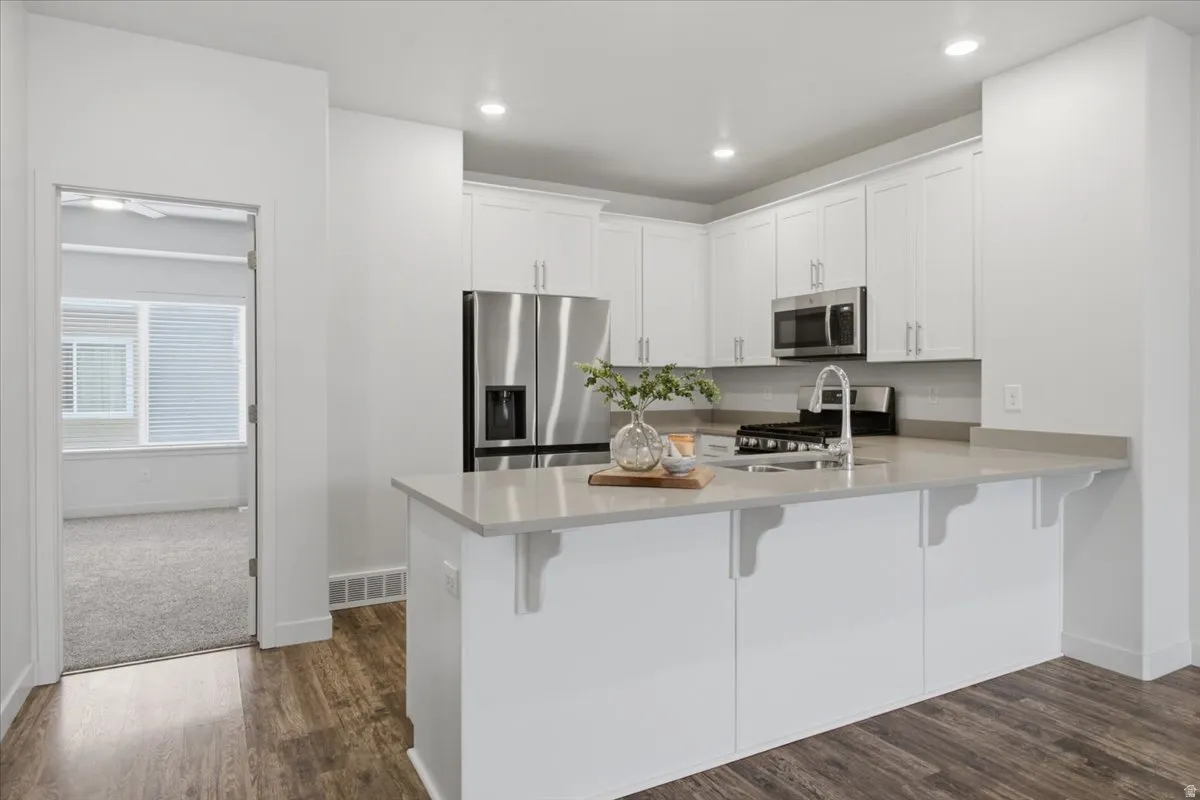 Kitchen featuring white cabinetry, stainless steel appliances, a center island with sink, neutral countertops, and wood-finish flooring