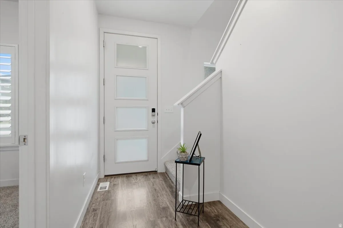 Entryway with wood-finish flooring, a modern front door with frosted glass panels, and a white staircase with a contemporary railing