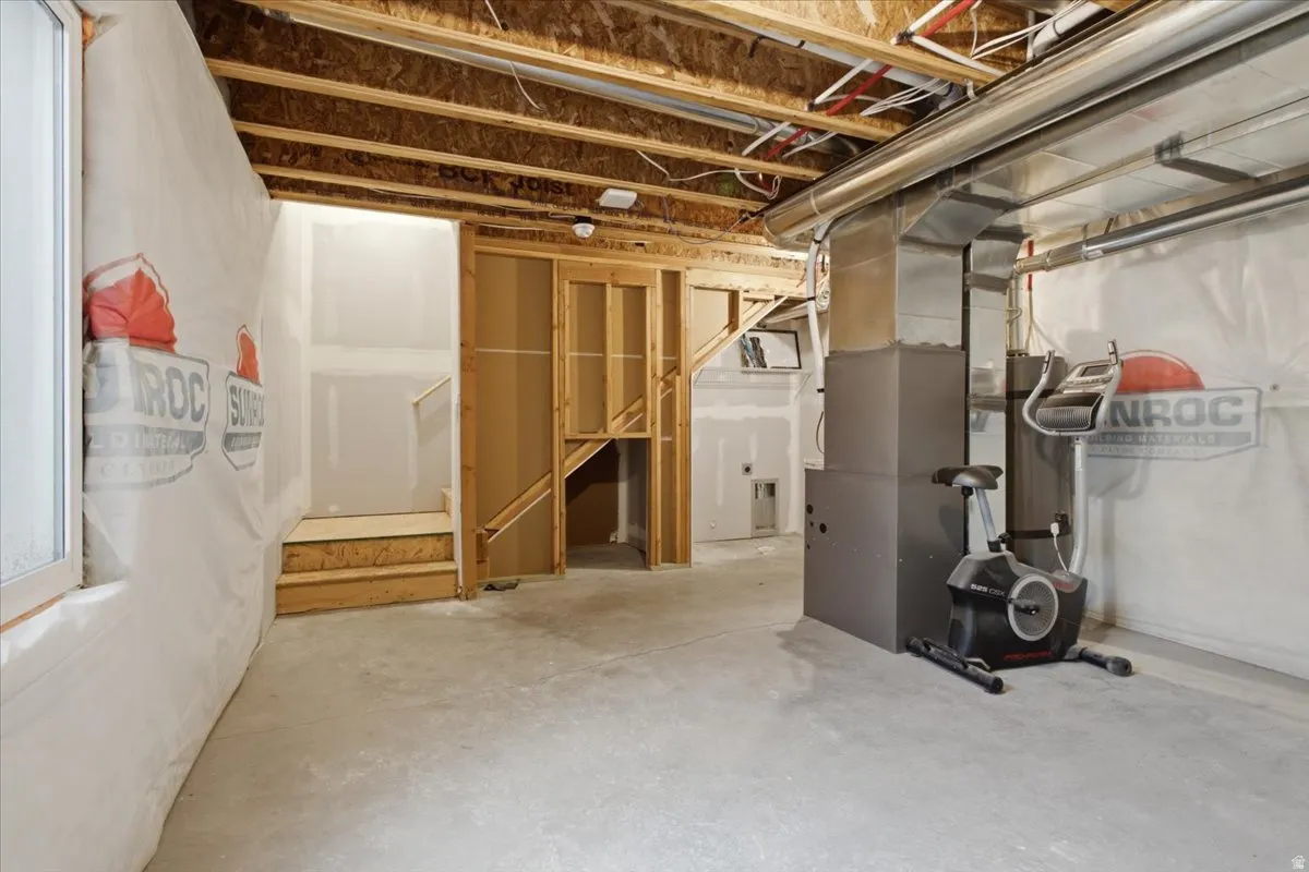 Unfinished basement space featuring exposed wood joists, concrete flooring, and a utility area with ductwork and a furnace