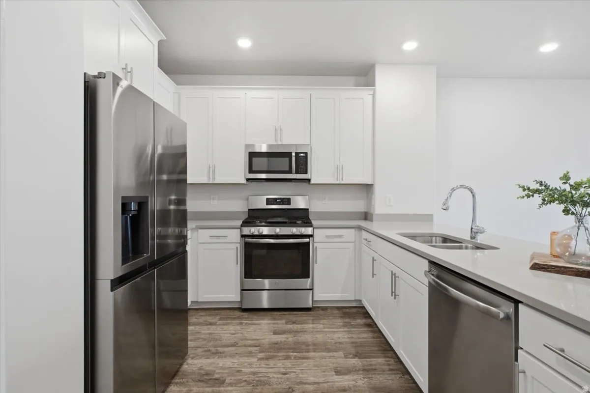 Kitchen featuring stainless steel appliances, white cabinetry, light countertops, and wood-finish flooring