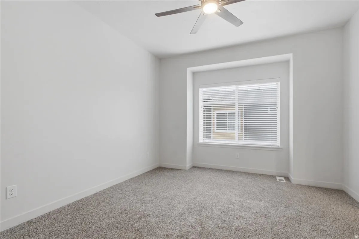 Recessed window with blinds, ceiling fan with integrated lighting, and neutral carpet flooring